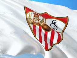 Colorful, wavy flag of Sevilla Fc, at blue sky on background