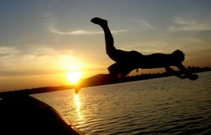 Silhouette of a man, jumping overboard, in the water, at colorful and beautiful sunset on background