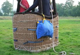 People in the basket of the hot air balloon, with the ballast, on the green meadow, near the trees