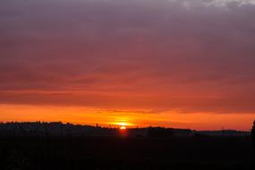 Beautiful and colorful sunset on horizon, with the clouds, above the landscape with the silhouettes