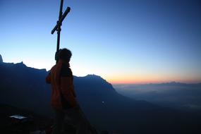 photo of a man and a cross on a mountain top