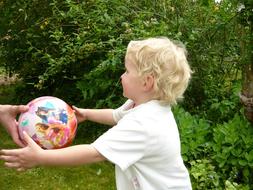 Blonde girl child playing with the colorful ball, among the colorful plants