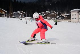 Person in bright jacket, doing ski boarding on the beautiful snow, near the houses, on the competition