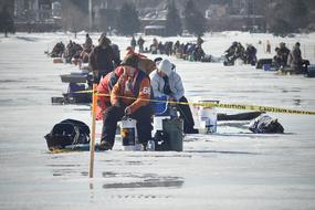 People, doing ice fishing on the beautiful, frozen lake, near the trees in Canada