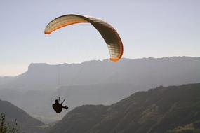 a man with a parachute is flying over the mountains