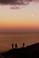 Silhouettes of the people, fishing near the water, at colorful and beautiful sunset on horizon