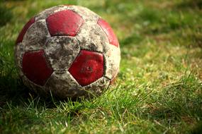 Old, dirty, red and white football, on the beautiful green meadow in light