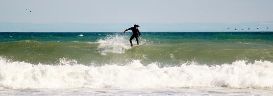 Surfer, surfing on the beautiful, green and blue sea, with the waves, at blue sky with clouds
