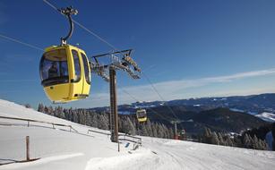 Yellow gondola, above the beautiful, snowy mountains with trees in winter, under the blue sky with white clouds