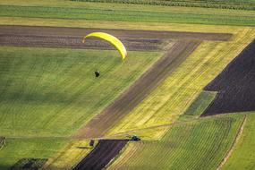 paraglider flies over green fields