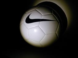 Close-up of the shiny, white "Nike" football ball, with the black logo, among the darkness