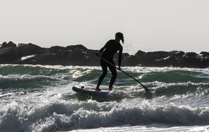 Silhouette of a surfer in wetsuit, with the paddle on the sea with waves