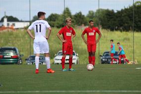 Football players, playing on the green field, with the fence, with the ball, near the cars and building