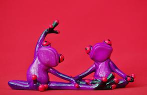 two purple figurines of frogs on a red background
