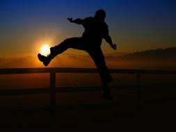 Silhouette of a person, running above the fence, at beautiful and colorful sunrise