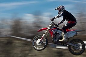 Side view of the motocross rider, in jump near the trees