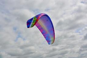 Colorful and beautiful paraglider wing, at blue sky with white and gray clouds on background, in France