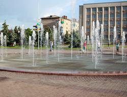 People, around the beautiful dancing fountain, near the plants and buildings