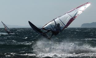 Person, jumping while doing windsurfing on the water, with the waves