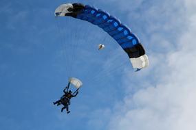 People, flying on the blue, black and white parachute, in the beautiful blue sky with white clouds