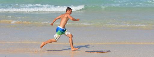 Wet man, in the colorful swimming shorts, running on the sandy beach near the beautiful ocean