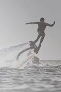 Black and white photo of a person on the flyboard, on the beautiful waterscape, at sky on background
