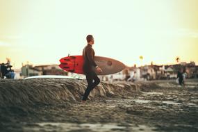 Man with the colorful surfboard, on the landscape, at beautiful sunset, on the beach