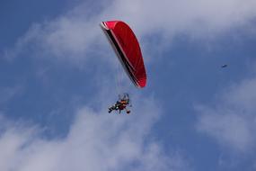 Paraglider, flying with the colorful parachute, in the blue sky with white clouds