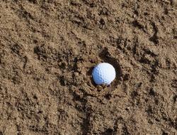 Shiny, white golf ball in the sand, in light