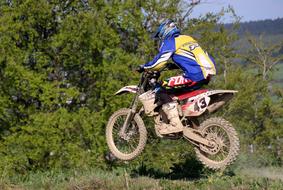 Motorcycle rider in the colorful uniform, in jump, among the beautiful and colorful plants