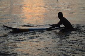Silhouette of a surfer with the surfboard, in the water, with ripple, in colorful and beautiful sunset in Bali, Indonesia