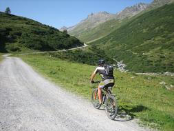 Person, cycling on the mountain bike, on the road, among the beautiful, green mountains, at blue sky on background