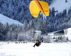 Paraglider on the yellow parachute, on the beautiful snowy mountain with trees and buildings in winter, in Switzerland