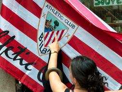 Woman, near the colorful flag, with the logo of "Bilbao" football club, and sign