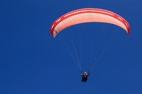 Person, flying on the red and white parachute, in the beautiful blue sky