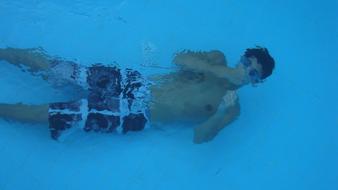 Man in shorts, diving in the blue swimming pool, above the tile