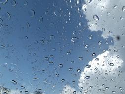 Beautiful water drops on the window, at blue sky with white clouds on background