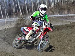 Motocross rider in the colorful equipment, on the colorful bike, on the landscape, near the trees