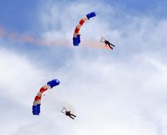 People with colorful parachutes, jumping from the airplane, in the beautiful blue sky with white clouds