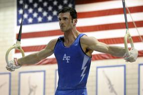 Athlete, doing exercise with the rings, at background with the flag of USA