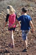 Girl and boy are walking along a colorful rocky road with plants