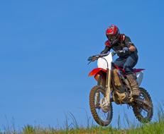 Man, on the colorful motorcycle, above the colorful grass, at beautiful blue sky on background, on the motocross competition