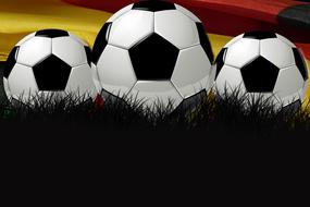 White and black footballs on the grass, at background with colorful flag of Germany on World Championship