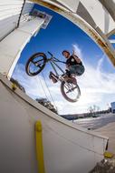 Person on the BMX bike in jump, at blue sky with white clouds on background