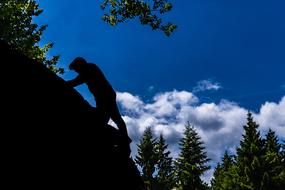 Silhouette of a climber on the rock, among the green trees of the beautiful Bavarian forest, at blue sky with white clouds on background, in Germany