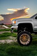 Side view of the shiny, metallic lifted car, on the beautiful landscape with the green grass, at beautiful and colorful sunset