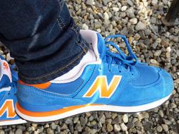 Blue, orange and white New Balance shoes on the person, above the stones