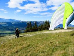 Person, doing paragliding with lime and white parachute, on the beautiful and colorful mountains