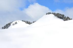 Beautiful, snowy mountains with the green trees, at blue sky with clouds on background