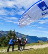 People doing paragliding with the white and blue parachute, on the beautiful, green mountains